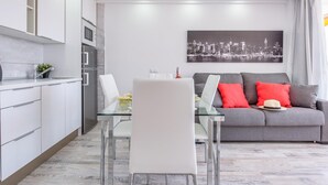 A modern living room with a grey sofa, a glass dining table, and a cityscape painting on the wall.