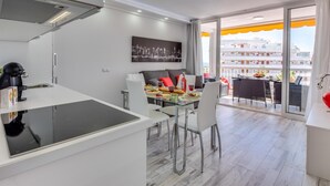 A modern kitchen with a built-in stove, dining area with a glass table, and a balcony with a view of buildings.
