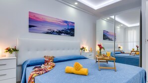A modern bedroom with a large bed, a bedside table with a lamp, a mirror, and a painting on the wall.