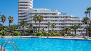 A hotel with a pool area, palm trees, and a multi-story building with balconies.