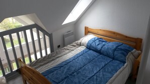 A bedroom with a sloped ceiling, a wooden bed frame, and a view of a green landscape through a window. - Duplex 5 people Carnac Beach with Feet (Carnac)