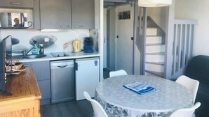 A compact kitchen with modern appliances, a dining area with a round table, and a staircase leading to another level. - Duplex 5 people Carnac Beach with Feet (Carnac)
