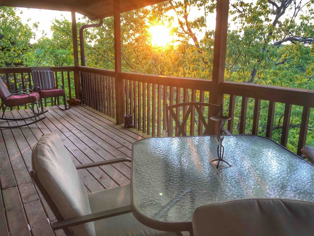 A covered outdoor area with a glass table and chairs, a cushioned bench, and a rocking chair.