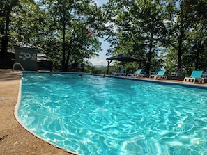 A swimming pool with clear water, surrounded by trees and a covered seating area.