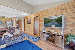 A cozy living room with a checkered sofa, a large flat-screen TV, and a wooden wall.