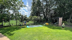 Een achtertuin met een trampoline, een klimmuur en een speeltoestel.