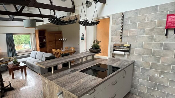 Een moderne keuken met een centraal eiland, inbouwapparatuur en een zithoek met een bank en stoelen.