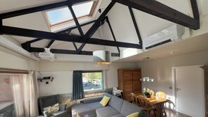 Een ruime woonkamer met een hoge plafond, een inbouwvuurplaats en een eethoek met houten meubels.