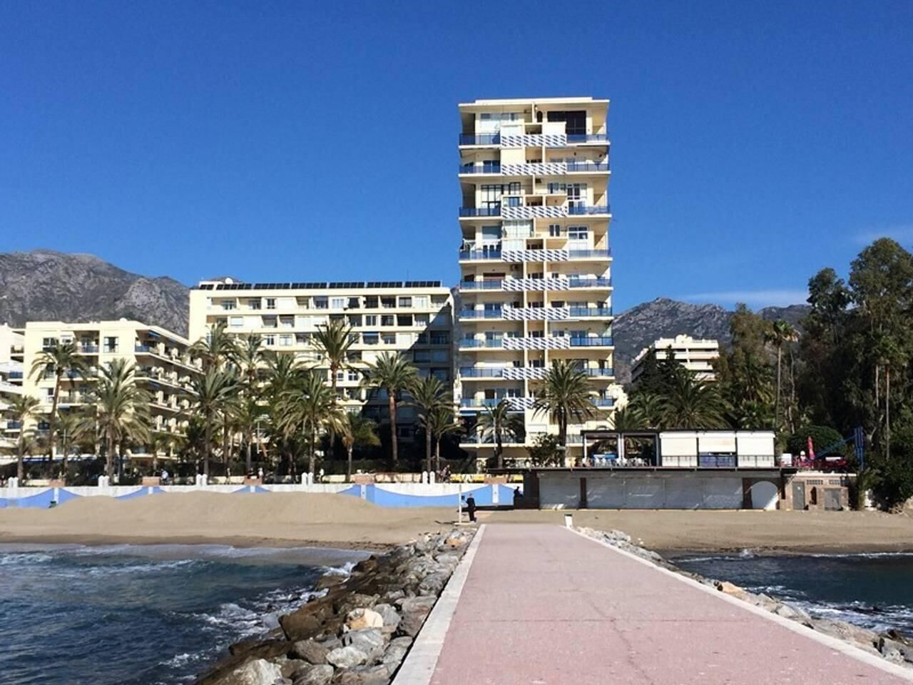 A beachfront hotel with multiple balconies, palm trees, and a clear view of the ocean.