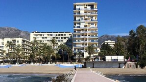 Ein Strandhotel mit mehreren Balkonen, Palmen und freiem Blick auf den Ozean.