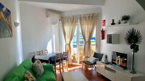 Ein modernes Wohnzimmer mit einem grünen Sofa, einem Esstisch mit Stühlen, einem Fernseher und einer kleinen Kommode.
