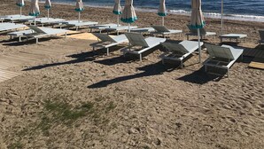 Ein Strand mit Reihen von Liegestühlen und Sonnenschirmen, ein klarer blauer Himmel und das Meer im Hintergrund.