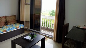 Une pièce comprenant un canapé, une petite table avec une télécommande et une plante, ainsi qu’un balcon doté d’une balustrade.