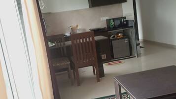 A living room with a sofa, a coffee table, a patterned rug, a dining area with a table and chairs, and a kitchen area with a microwave and a TV.