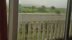 Un balcon doté d’une balustrade blanche, qui offre une vue sur un paysage verdoyant, avec des arbres et des collines.