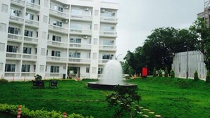 Un immeuble à plusieurs étages doté d’une cour intérieure, d’une fontaine et d’une personne qui travaille sur la pelouse.