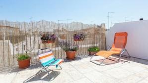 Une terrasse sur le toit, avec deux chaises longues, une clôture en bambou et des plantes en pot.