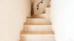 Un escalier recouvert de carreaux beiges, une petite plante accrochée au mur et une main courante noire.