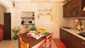 Une cuisine compacte avec des meubles en bois, une table à manger avec des chaises et un petit îlot central où sont disposés des fruits et des légumes.