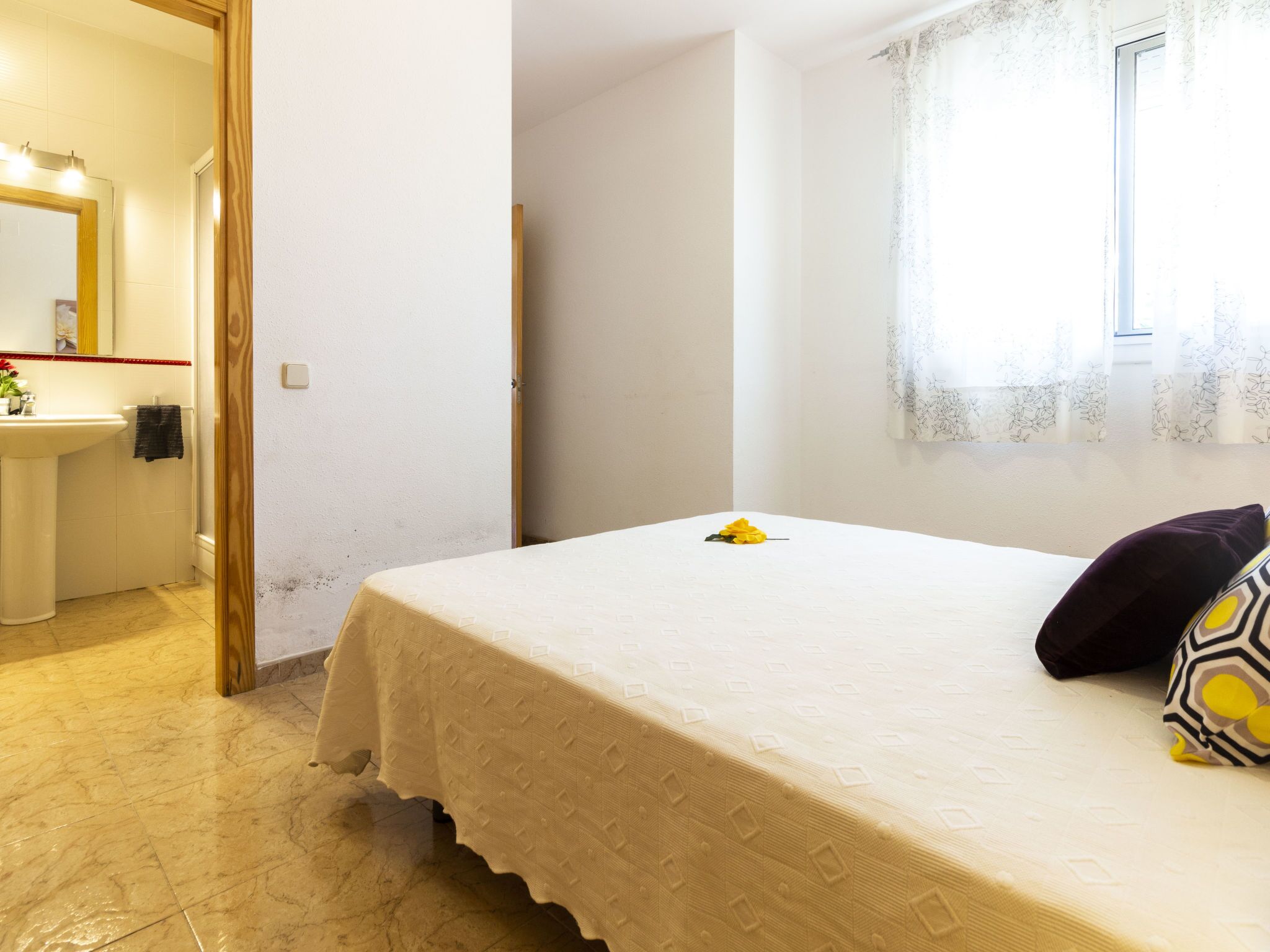 Un dormitori amb llit, finestra amb cortina, bany amb banyera i mirall, i una porta.
