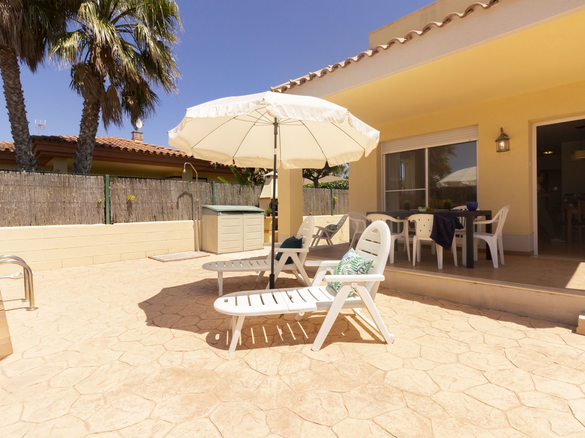 An outdoor patio with a white umbrella, two lounge chairs, and a table.