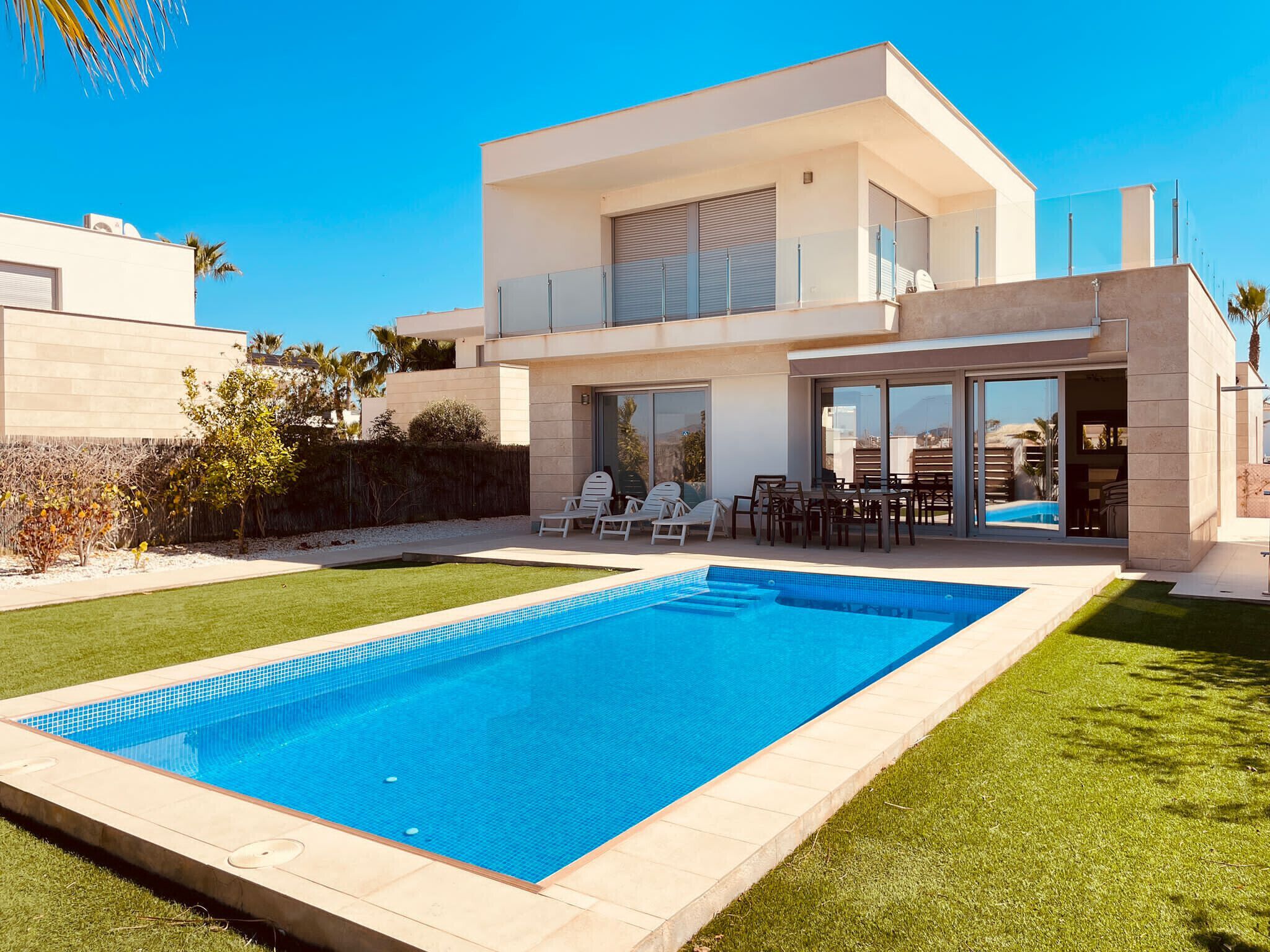 A modern two-story house with a swimming pool, outdoor seating, and a well-maintained lawn.