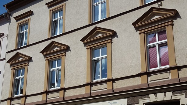 A building with multiple windows, a storefront with a sign, and a black ornate door. - Apartment Hahn Sebnitz (Sebnitz)