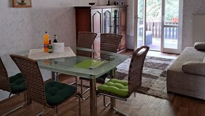 A dining area with a glass table, wicker chairs, and a green cushion. There is a cabinet with a radio and a lamp on top. A framed picture hangs on the wall. - Apartment Hahn Sebnitz (Sebnitz)