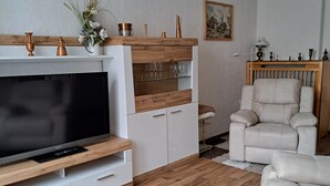 A living room with a flat-screen TV, wooden cabinets, a sofa, and a chair. - Apartment Hahn Sebnitz (Sebnitz)