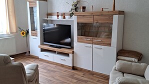 A modern living room with a flat-screen TV, wooden cabinets, and a glass display shelf. - Apartment Hahn Sebnitz (Sebnitz)