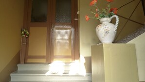 A wooden door with a glass panel, a white vase with orange flowers on a white pedestal, and a small wreath on the left. - Apartment Hahn Sebnitz (Sebnitz)