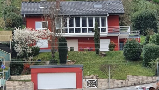 A two-story house with a red and white exterior, a garage, and a small garden with flowering plants. - Beautiful apartment Casa Rossa in Neckarsteinach am Neckar. (Neckarsteinach)