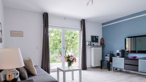 A modern living room with a sofa, a small table with a vase, a TV, and a radiator.