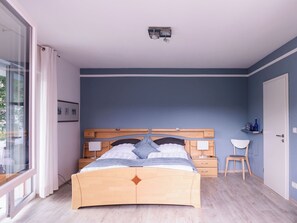 A bedroom with a bed, bedside tables, a chair, a window, and a door. - Beautiful apartment Casa Rossa in Neckarsteinach am Neckar. (Neckarsteinach)