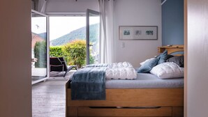 A bedroom with a wooden bed, a view of greenery and hills, and a chair by the window.