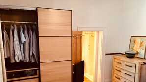 A bedroom with a wooden wardrobe, a bedside table with a bowl, and a door leading to a bathroom. - Napier Cottage - Cozy Hills Retreat (Hawthorndene)