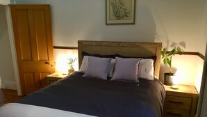 A bedroom with a bed, two bedside tables, a nightstand, a wooden door, and a potted plant. - Napier Cottage - Cozy Hills Retreat (Hawthorndene)