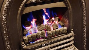A fireplace with a decorative surround and a fire burning inside. - Napier Cottage - Cozy Hills Retreat (Hawthorndene)