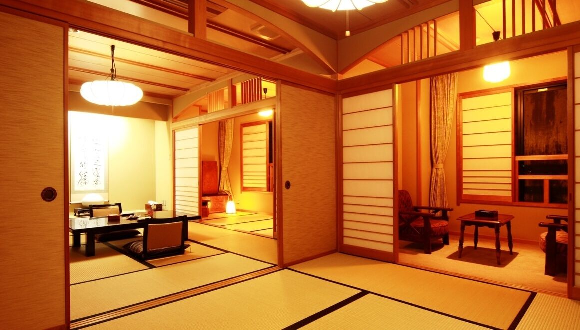 Ein traditioneller japanischer Raum mit Tatami-Böden, Schiebetüren, einem niedrigen Tisch mit Kissen und einer hängenden Leuchte.