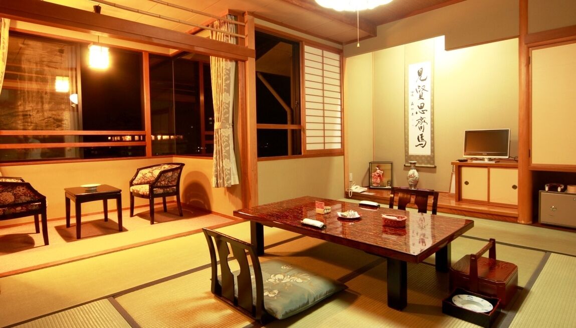 Une pièce de style japonais traditionnel, avec un sol recouvert de tatamis, une table basse avec des coussins, un téléviseur et des portes coulissantes.