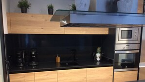 Eine moderne Küche mit schwarzem Arbeitsplatz, Holzschränken, einer Glasrückwand, einem Einbauofen und einer Kaffeemaschine.