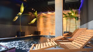 Un espace piscine agrémenté de chaises longues en bois, d’un élément décoratif aquatique et de grandes plantes.