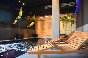 Ein Poolbereich mit Holzliegen, einem Wasserspiel und großen Pflanzen.