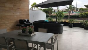 Eine Terrasse mit Esstisch, Stühlen, Grill, einer Sitzecke und Kübelpflanzen.