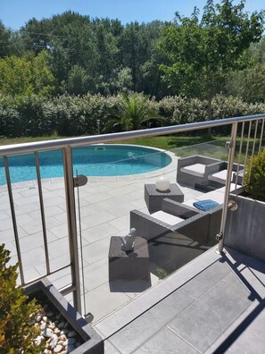 A swimming pool with a glass barrier, surrounded by outdoor seating and a landscaped garden.