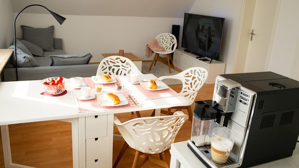 A modern living room with a dining table set for breakfast, a coffee machine, and a flat-screen TV. - Beautiful new, modern apartment in Grömitz, 43sqm (Grömitz)
