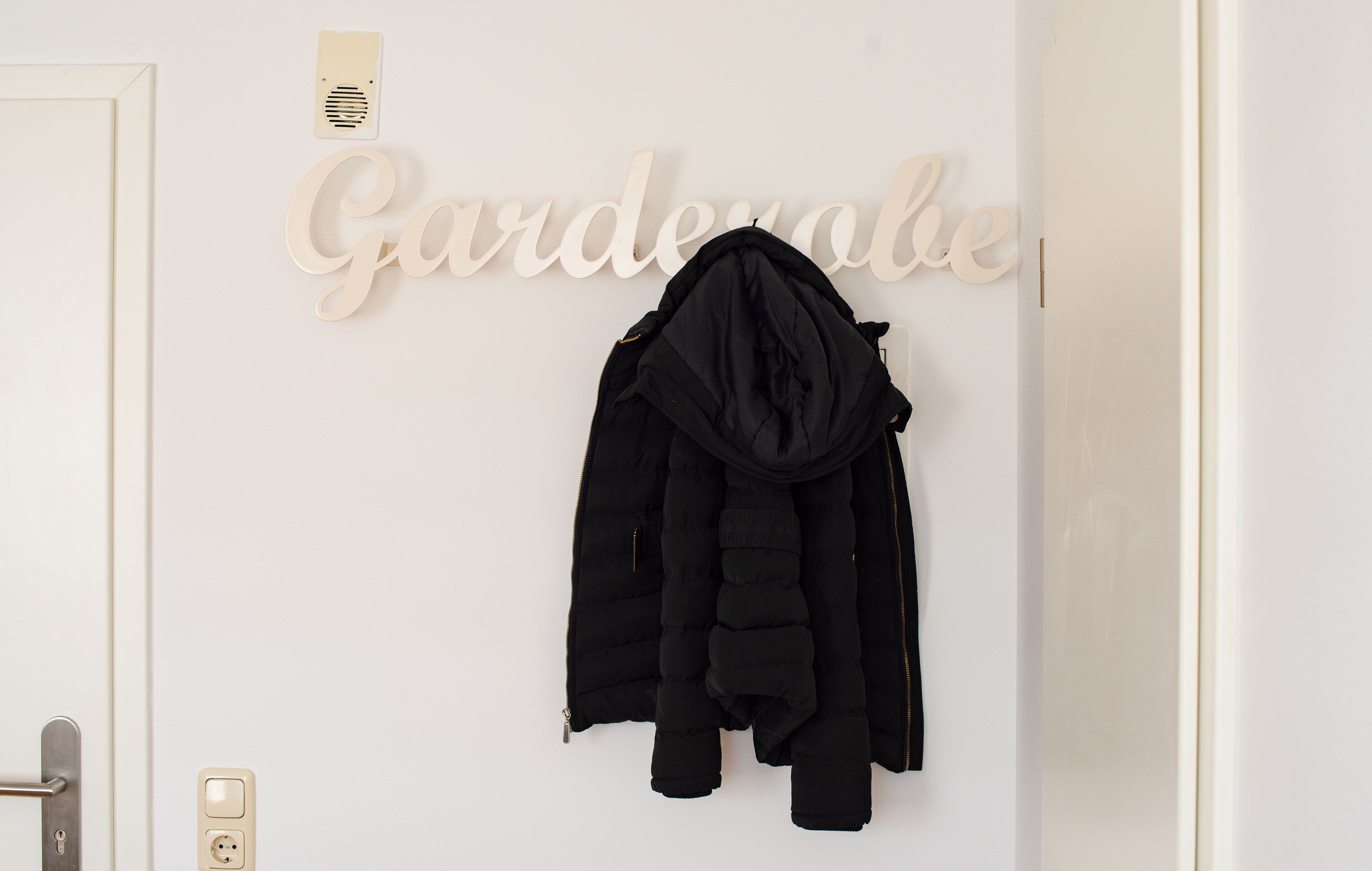 Une porte blanche avec un porte-manteau sur lequel sont accrochés un blouson noir et un chapeau noir.