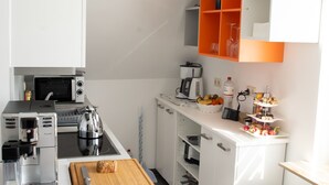 A modern kitchen with white cabinetry, a wooden cutting board, a kettle, a coffee maker, and a fruit bowl. - Beautiful new, modern apartment in Grömitz, 43sqm (Grömitz)