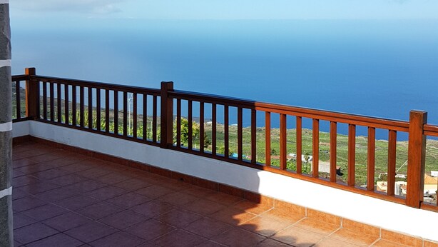 Eine Terrasse mit Holzgeländer, einer Steinmauer und Blick auf das Meer.