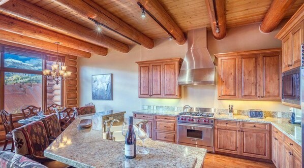 A spacious kitchen with wooden cabinets, granite countertops, and a large island with seating. - Townhomes On The Creek 121 (Mountain Village)